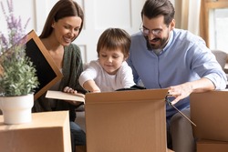 Happy young Caucasian family unpack unbox packages relocate to new house or apartment together. Smiling mom and dad enjoy settling moving to own home with little son child. Rental, mortgage concept.