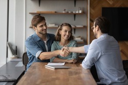 Smiling young couple buyers shake and get acquainted greet with relator or broker at office meeting. Happy man and woman clients handshake close deal or make agreement with real estate agent.