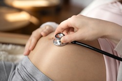 Crop close up of doctor hold stethoscope listen to pregnant woman baby bump, check kid in womb. Nurse or gynecologist use phonendoscope examine child in belly heartbeat. Pregnancy concept.