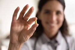 Pharmacological therapy. Close up portrait of smiling female doctor scientist pharmacist looking at camera presenting new effective pill medicine. Focus on yellow capsule in woman medical worker hand