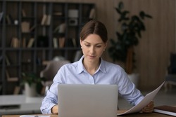 Computer and papers. Focused millennial woman office worker teacher freelancer do paperwork manage legal documents fill in electronic form. Young lady lawyer study text of contract agreement by laptop