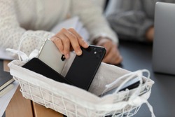 Close up cropped of young woman employee businesswoman putting phone in basket, involed in meeting with colleague, free from smartphone, no cellphone zone in office or digital detox concept