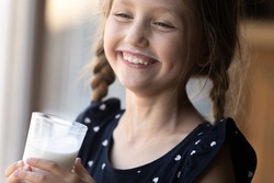 Happy girl with funny moustache drinking milk, holding glass, smiling and laughing. Positive child keeping healthy nutrition, getting calcium and vitamins from for growth from dairy products