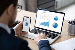 Business marketer using professional app for marketing data analyzing on laptop and smartphone screens, studying financial graphs, comparing diagrams on phone and computer. Analysis concept