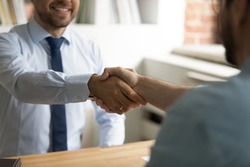 Close up happy two business men shaking hands, coming to agreement after negotiations meeting. Smiling employer welcoming job applicant at interview in office, making offer, recruitment concept.