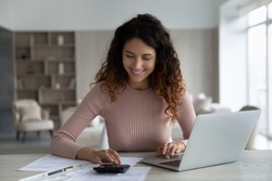 Smiling young Hispanic woman manage household family budget pay bills taxes on laptop online. Happy Latino female calculate expenditures expenses on machine, take care of finances or savings.