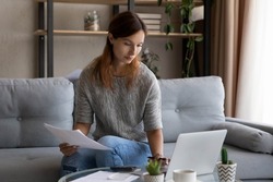 Confident woman calculating expenses or domestic bills, checking financial documents, sitting on couch at home, focused young female using laptop and calculator, managing planning household budget