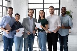 Portrait of happy diverse group of interns or students and corporate teacher after successfully passes exam. Multi ethnic business team of employees holding paper documents, looking at camera, smiling