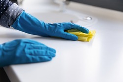 Housewife, cleaner, janitor wearing blue protective rubber gloves, washing table top or kitchen counter white surface with rag. Close up of hands. Household, cleaning service, domestic work concept