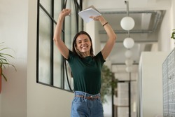 Happy excited student celebrating success, passed exam, high test grade, good result. Millennial girl feeling joy, dancing in office corridor. Candidate getting hired after successful job interview