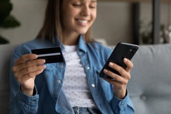 Young woman holding credit card and smartphone enjoy ecommerce online services, close up focus on device and card. Secure e-banking, transfer money through mobile app, easy comfort shopping concept