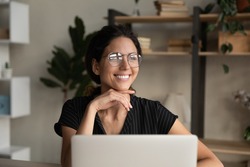 Close up dreamy smiling businesswoman in glasses distracted from laptop, looking to aside, pensive young woman visualizing good future, dreaming about new opportunities, pondering project strategy