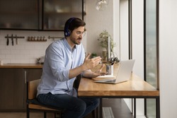 Man sit in kitchen wear headphones communicates through videoconference use laptop working remotely from homeoffice. Provide help, explanation and support to client distantly, video call event concept
