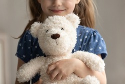 Close up of teddy bear in arms of child. Happy smiling little girl kid holding, hugging toy, playing with plush soft friend. Cropped portrait. Childhood, preschooler, playtime, childcare concept