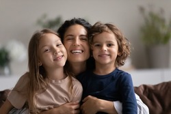Portrait of happy mother hugging two cute little kids. Joyful affectionate mom cuddling sweet sibling son and daughter, looking at camera with toothy smile. Family relationship, motherhood. Head shot