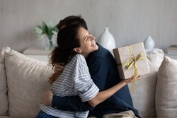 Happy young 30s latina woman embracing loving husband, feeling thankful for getting present in wrapped gift box, celebrating happy birthday or marriage anniversary, international women s day.