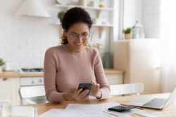 Smiling young Caucasian woman manage household budget finances paying bills taxes on smartphone online. Happy female busy with documents calculate expenses expenditures on cellphone on internet.