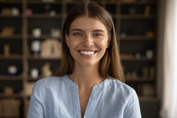Happy attractive teen student girl home head shot portrait. Young millennial woman with natural makeup wearing pale linen shirt, smiling at camera, showing white perfect healthy teeth. Front view