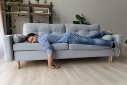 Exhausted young man fell asleep on comfortable couch in modern living room, having no energy after hard working day. Tired depressed unmotivated caucasian guy napping on sofa at home, fatigue concept.