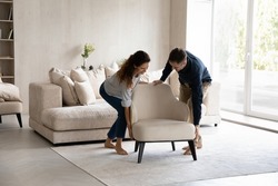 Spouses carrying modern armchair, placing furniture relocating into new home. Happy homeowners 35s couple enjoy moving day, start new life at own house. Fashionable apartment owners, bank loan concept