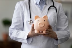 Crop close up female doctor physician nurse wearing white uniform with stethoscope holding pink piggy bank, medical insurance concept, healthcare and medicine, hospital budget, clinic fees