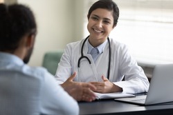 Smiling young Indian woman doctor consulting African American patient at meeting in hospital, friendly female physician practitioner talking, giving recommendation, discussing checkup or symptoms