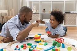 Proud dad and happy little son bumping fists over toy blocks and railway model on heating floor. Father giving praise to kid, expressing approval, enjoying friendship, fatherhood, playtime