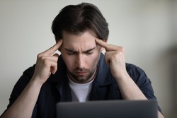 Concentrated serious young employee man holding head, touching templates with fingers with closed eyes, thinking over project issue decision hard, feeling headache, migraine, tiredness, fatigue