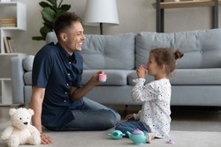 Cheerful daddy and sweet happy preschool daughter kid playing tea party, pretending drinking coffee, tea from toy cups, using plastic dish, enjoying game, playtime, family leisure time