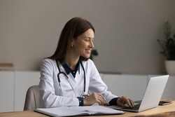 Modern tech for healthcare. Smiling female doctor sit at desk use laptop watch professional training webinar online manage electronic medical document. Young woman gp work on computer in clinic office