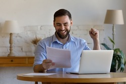 Emotional laughing happy young man looking at paper document, feeling excited reading amazing news, getting dream job offer, profitable deal or bank loan approvement, celebrating success at home.