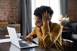 Unhappy confused millennial African American woman in glasses looking at laptop screen, stuck with difficult task or feeling stressed working with electronic documents, reading email with bad news.