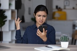 Upset annoyed Indian girl having problems with smartphone, looking at screen, feeling frustrated, angry, disappointed. Mobile phone user woman getting bad connection, spam, app work errors