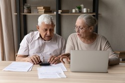 Concentrated middle aged mature family couple calculating domestic expenditures or taxes, managing monthly budget, paying taxes or bills in computer e-banking application, planning investment.