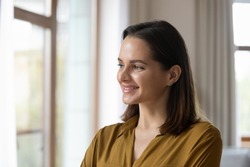 Happy thoughtful millennial business woman in casual looking at window with pensive dreamy smile, thinking of work project future vision, ambitious career, planning goals. Head shot portrait
