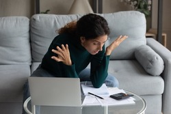 Unhappy anxious millennial gen latin woman feeling stressed calculating domestic expenses or managing monthly budget using computer at home, suffering from lack of money or having financial problems.