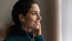 Close up head shot young attractive woman listening favorite popular music in wired earphones, looking in distance, daydreaming or enjoying peaceful calm weekend pastime alone at home, hobby activity.