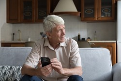 Worried senior smartphone user getting bad, concerning news message, holding mobile phone, looking away, feeling stressed, anxious, thinking over problems, sms answer
