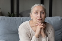 Sad lonely pensive elder lady looking away, sitting on couch at home with chin on hands, thinking over health problems, feeling sadness, boredom, apathy, concerned about memory loss, dementia