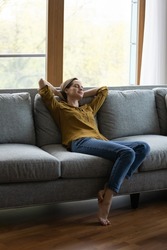 Vertical view serene woman relax on sofa with eyes closed and hands behind head enjoy carefree day off, breath fresh air, climate control inside for comfort living. Tenant, modern smart house concept