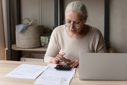 Personal finances management, accounting concept. Older woman in glasses sitting at table using calculator make arithmetic operations, calculates monthly costs, control family budget, analyze expenses