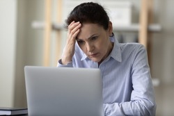 Shocked puzzled mature business lady reading bad news on Internet, touching head, feeling stress, headache, thinking over problems hard, looking at laptop screen, making difficult decision