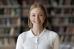 Head shot young beautiful teenager girl smile looking at camera. Blond 18s student posing in university library, concept of higher education, high school excellent pupil portrait, studentship concept