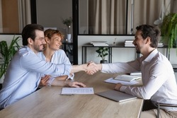 Confident lawyer meeting and shaking hands with happy couple of clients. Husband and wife visiting office of mortgage broker, real estate agent, house seller shaking hands over signed contract