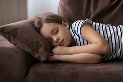 Sweet dreams. Cute little preteen girl sleep dream nap on cozy couch lying in comfortable pose with closed eyes. Tired tween child kid fall asleep on comfy sofa in silent living room after active day