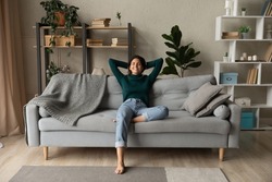 Sweet idleness. Lazy young hispanic lady sit in relaxed pose on big comfy sofa at living room interior breath air dream imagine. Successful female new flat apartment buyer rest at home feel pleasure