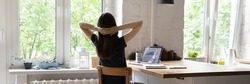 Panoramic image rear view female analyst worker sit at desk with hands behind head rest after productive work on laptop, looks out window. No stress, success, results, take break at workplace concept