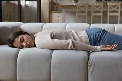 Tired calm young woman resting on spacious sofa in home living room, lying on belly, sleeping at daytime, feeling fatigue after stress, sleepless night. Leisure time, recovery concept