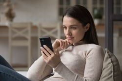 Focused millennial woman using mobile phone at home, reading online content, browsing internet, shopping with application. Gen Z girl texting message on chat on cellphone at home
