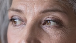 Close up cropped wrinkled front face view of attractive brown-eyed older woman staring into distance looking pensive and thoughtful. Eyes vision check up clinic ad services for older citizen concept